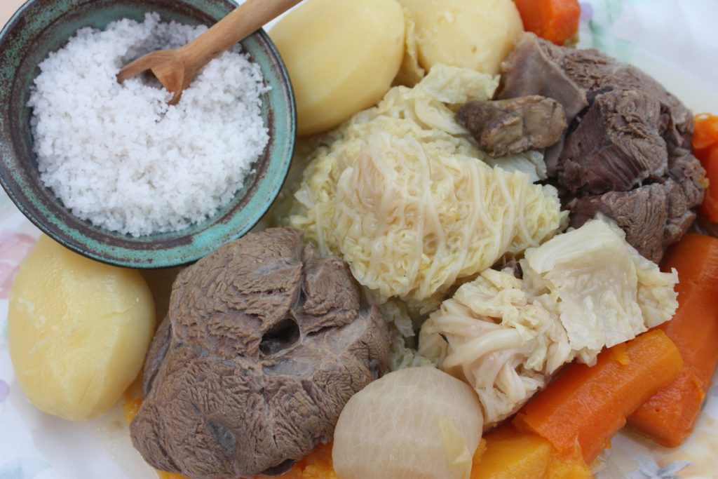 Ein Teller mit gegartem Rindfleisch, Wirsing, Karotten und Salzkartoffeln neben einer Schale grobem Salz.