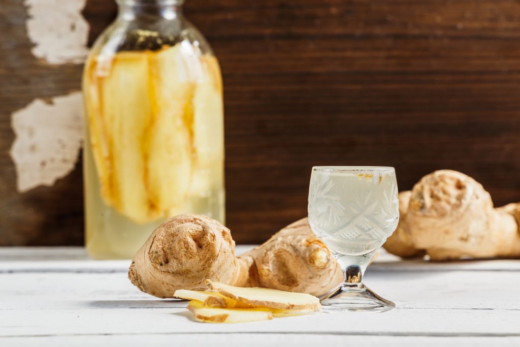 Eine Hand gießt die fertige, leuchtend gelbe Goldene Ingwer-Essenz durch einen Glastrichter in eine kleine Apothekerflasche.