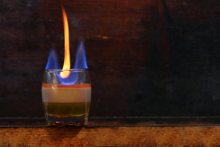 Ein einzelnes Shotglas mit einem brennenden B52, wobei eine hohe orange-blaue Flamme von der obersten Schicht aufsteigt.