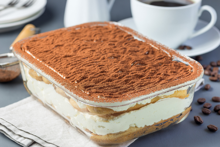 Eine große Glasform gefüllt mit geschichtetem Tiramisu, dessen Oberfläche dicht mit Kakaopulver bestreut ist.