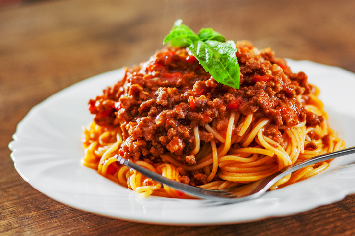 Ein Teller Spaghetti ist mit reichlich Bolognesesauce und einem Basilikumblatt angerichtet.