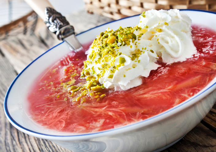 Eine Schüssel mit leuchtend rotem Rhabarberkompott, getoppt mit Sahnetupfern und gehackten Pistazien.