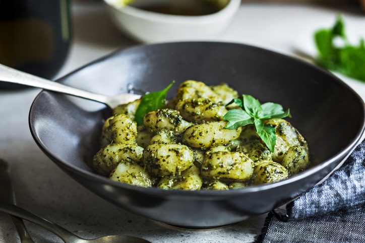 Eine dunkle Schüssel gefüllt mit Gnocchi, die großzügig mit grobem Basilikum-Pesto überzogen und mit frischen Basilikumblättern garniert sind.