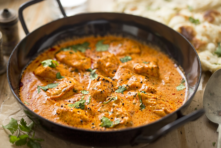 Mehrere Stücke Butter Chicken liegen in einer cremigen orangefarbenen Sauce in einer großen Pfanne.
