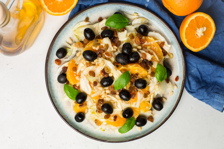 Ein Teller mit Orangen-Fenchel-Salat, bestreut mit Rosinen, Pinienkernen und frischen Basilikumblättern.