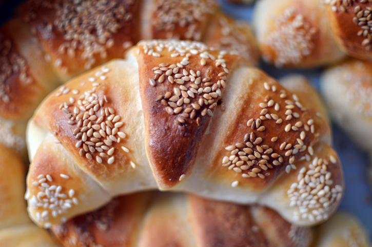 Ein einzelnes, goldbraun gebackenes Croissant mit reichlich Sesam bestreut.