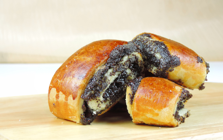 Aufgeschnittene saftige Mohnrollen mit dunkler Füllung liegen auf einem hellen Holzbrett.