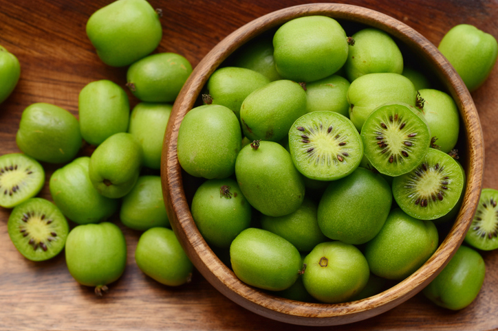 Eine Holzschale ist mit kleinen grünen Mini-Kiwis gefüllt, von denen einige aufgeschnitten sind.