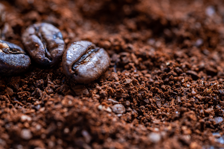 Eine Makroaufnahme von drei ganzen Kaffeebohnen, die auf einem Haufen fein gemahlenem Kaffeepulver liegen.