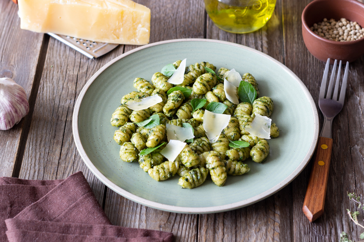 Gnocchi mit Pesto und Parmesan auf einem Keramikteller, im Hintergrund ein Stück Grana Padano und eine Reibe auf dunklem Holz.