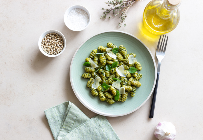 Frische Gnocchi in grünem Basilikum-Pesto, garniert mit Parmesan-Hobeln und Minzblättern auf einem mintgrünen Teller.