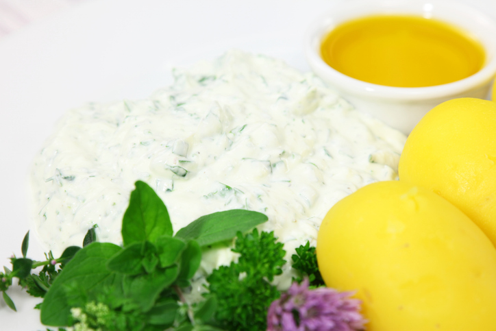 Nahaufnahme von cremigem Quark mit Kräutern, daneben frische Petersilie, Oregano und Leinöl.