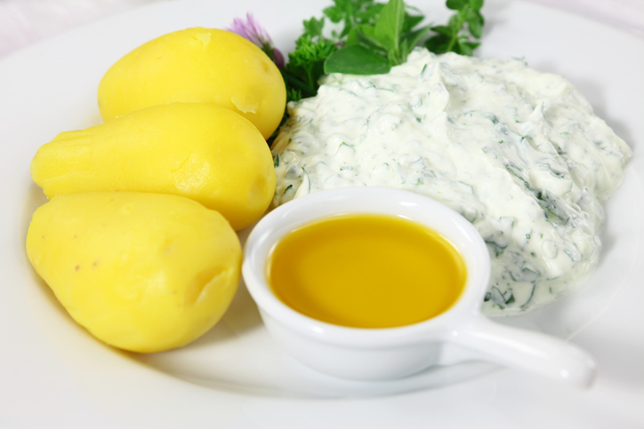 Drei geschälte Pellkartoffeln auf einem weißen Teller neben Quark und einer kleinen Schale Leinöl.