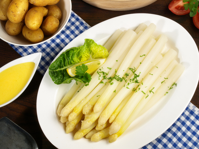 Weißer Spargel liegt auf einem großen Teller mit Kartoffeln, Zitrone und Sauce.