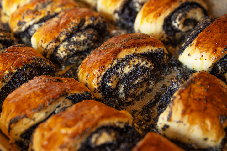 Mehrere saftige Mohnrollen mit dunkler Mohnfüllung liegen dicht nebeneinander auf einem Blech.