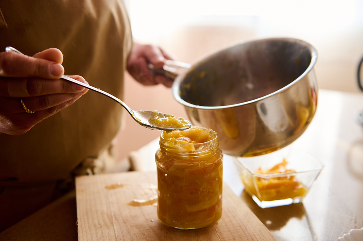 Frische Orangenmarmelade wird mit einem Löffel aus einem Topf in ein Glas gefüllt.
