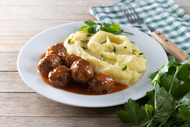 Ein Teller mit Frikadellen in Soße und Kartoffelpüree ist mit etwas Petersilie garniert.