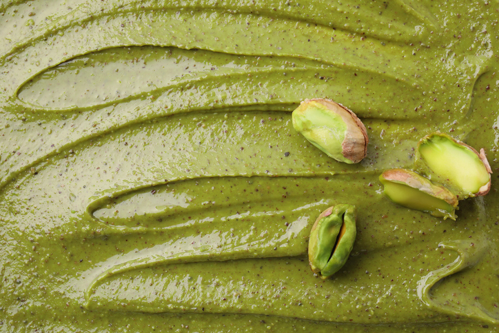 Eine glatte Fläche aus Pistaziencreme ist nah zu sehen und mit einigen Pistazien dekoriert.