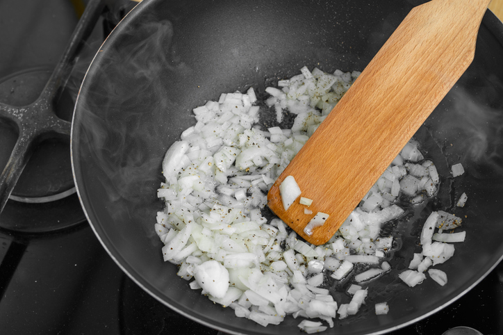 Kleine Stücke von Zwiebel werden in einer Pfanne mit einem Holzspatel angebraten.
