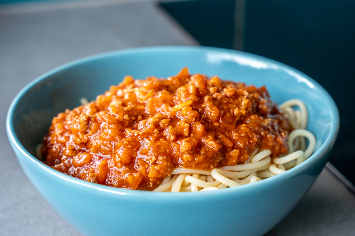 Eine blaue Schüssel ist mit Spaghetti und einer dicken Bolognesesauce gefüllt.