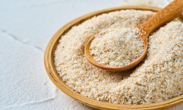 Ein Holzlöffel liegt auf einem Teller voller heller Flohsamenschalen.