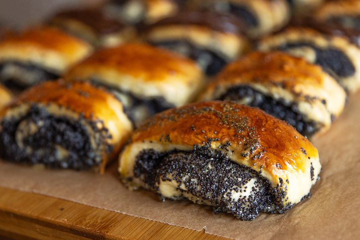 Kleine saftige Mohnrollen mit glänzender Kruste liegen frisch gebacken auf Backpapier.