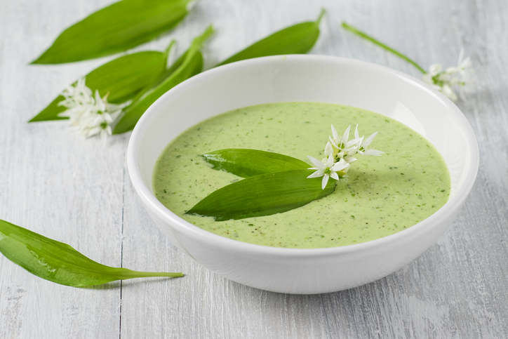 Eine helle grüne Bärlauchsuppe steht in einer weißen Schale und ist mit Bärlauchblättern dekoriert.