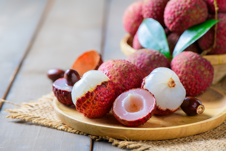 Mehrere Litschis liegen teils geschält und teils geöffnet auf einem runden Holztablett.