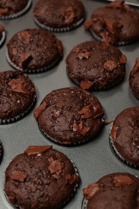 Dunkle Schokoladen-Muffins mit Schokostücken liegen in einer Muffinform.