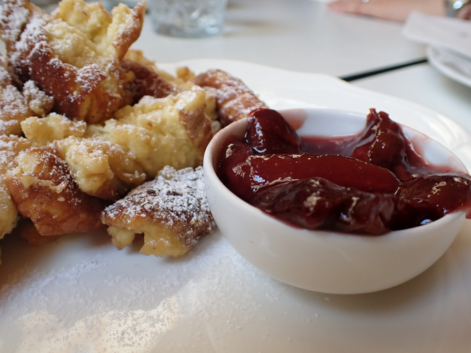 Goldbraun gebackene, mit Puderzucker bestreute Kaiserschmarrn-Stücke neben einer kleinen weißen Schale mit dunklem Zwetschkenkompott.