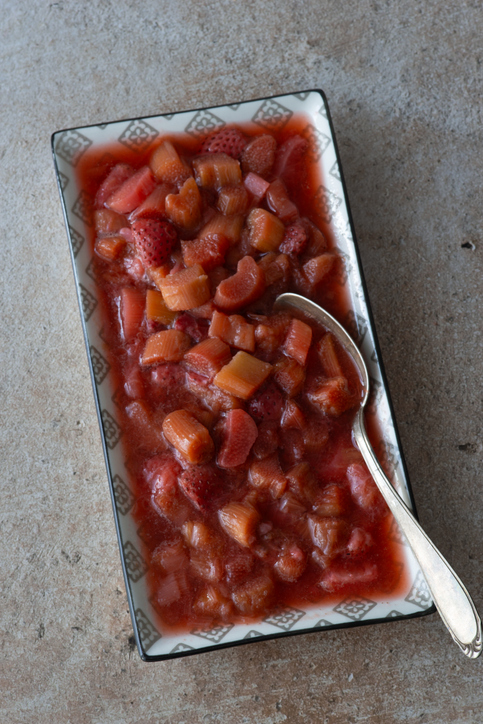 Eine rechteckige Servierschale mit einer Mischung aus gekochtem Rhabarber und ganzen Erdbeeren in einem roten Fruchtspiegel.