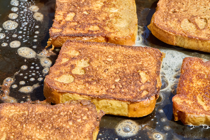 Mehrere Scheiben French Toast braten goldbraun in Butter auf einer heißen Fläche.