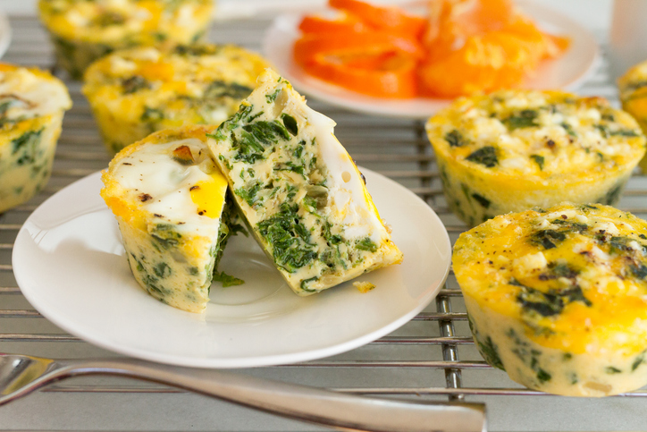 Ein halbierter Frittata-Eiermuffin liegt auf einem kleinen Teller neben weiteren Eiermuffins.