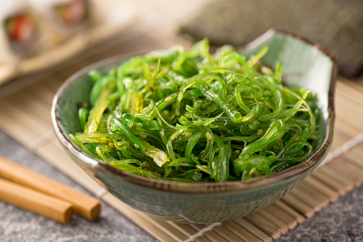 Leuchtend grüner Wakame-Salat mit Chili-Flocken und Sesam in einer grünlich-braunen Schale.