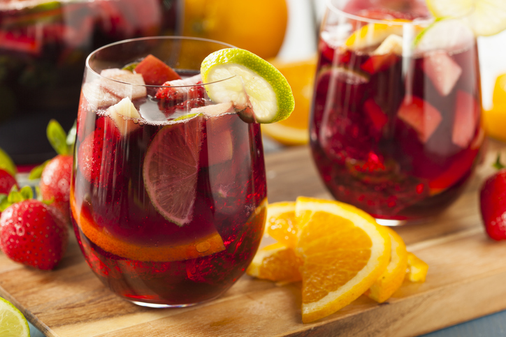 Zwei Gläser Sangria mit Früchten stehen neben Orangenscheiben und Erdbeeren auf einem Holzbrett.