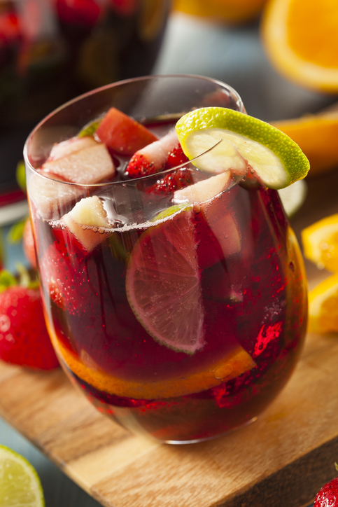 Ein Glas Sangria mit Erdbeeren, Limette und Orangenscheiben steht auf einem Holzbrett.