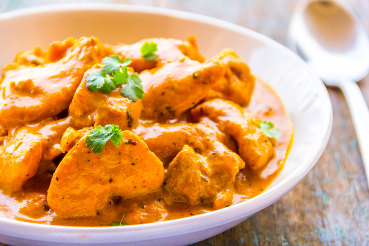Zarte Hähnchenstücke liegen in einer cremigen orangefarbenen Butter-Chicken-Sauce in einer weißen Schale.