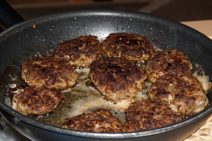 Mehrere kräftig gebräunte Frikadellen braten in einer Pfanne in heißem Fett weiter.