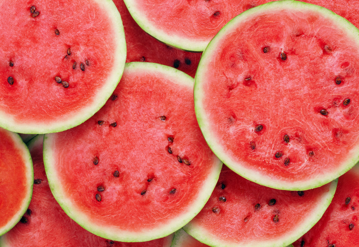 Viele runde, saftige Scheiben einer roten Wassermelone liegen dicht beieinander.