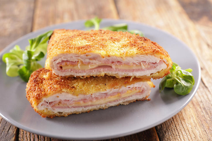 Zwei Hälften eines goldbraun gebackenen Cordon Bleu vom Huhn liegen auf einem grauen Teller, garniert mit frischem Feldsalat.