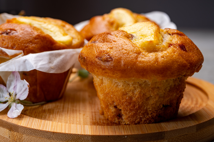 Frische Apfel-Zimt-Muffins stehen auf einem runden Holzbrett, verziert mit einem zarten Blütenzweig.