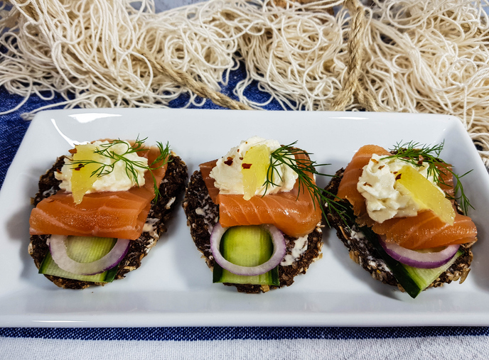 Drei Lachs-Schnittchen auf einem weißen Teller, garniert mit Meerrettich-Creme und einem Stück Zitrone.