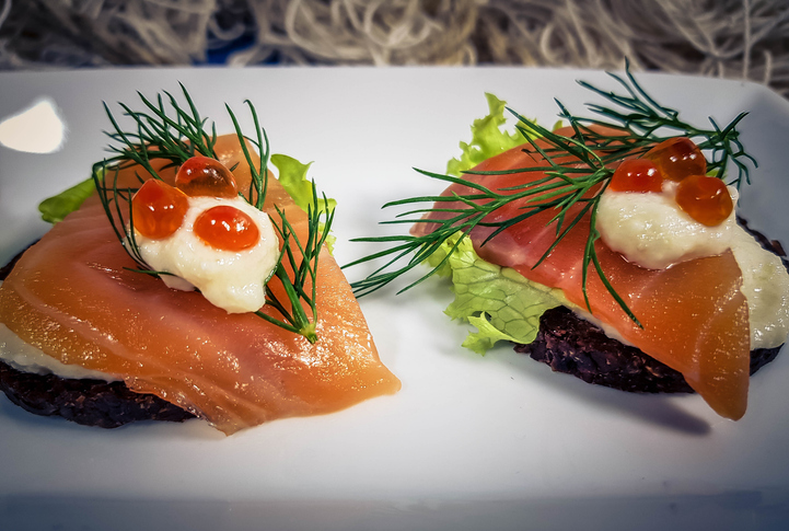 Zwei Lachs-Schnittchen auf dunklem Pumpernickel, getoppt mit Rogen und frischem Dill.