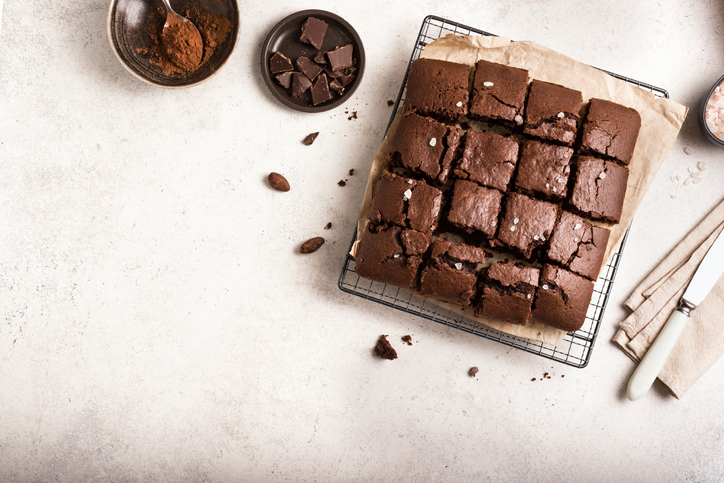 Draufsicht auf ein ganzes Blech Brownies, das in Quadrate geschnitten auf Backpapier liegt und mit groben Meersalzkörnern bestreut ist.