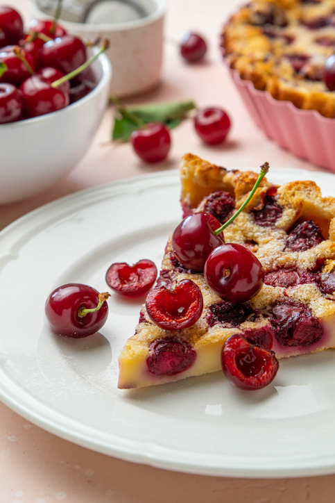 Ein einzelnes Stück einer saftigen Clafoutis mit Kirschen liegt auf einem weißen Teller.