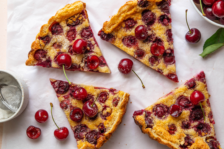Mehrere Stücke einer Clafoutis mit Kirschen sind dekorativ auf Backpapier angerichtet.