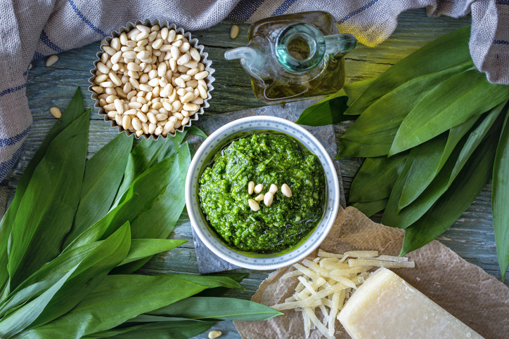Eine Schale mit Bärlauchpesto umgeben von Pinienkernen, Parmesan und Bärlauchblättern.