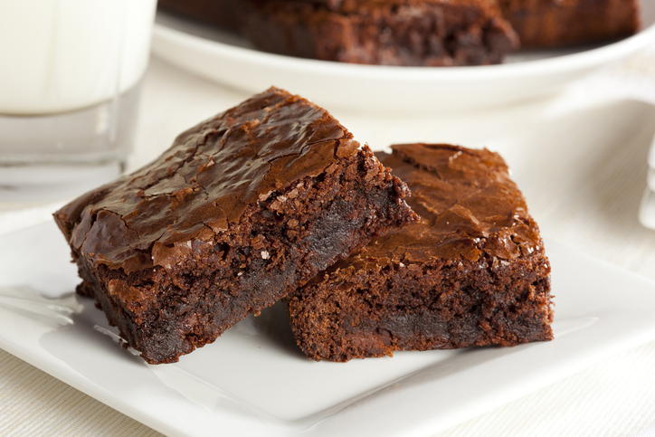 Zwei saftige Schokoladenbrownies übereinander auf einem weißen Porzellanteller, daneben ein Glas Milch.