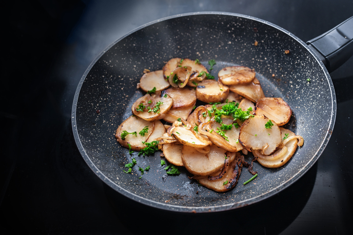 Goldbraun gebratene Topinambur-Scheiben mit Zwiebeln und frischer Petersilie in einer dunklen Bratpfanne.