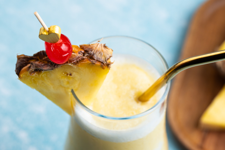 Nahaufnahme einer Pina Colada mit einer Ananasscheibe und einer Cocktailkirsche an einem goldenen Herz-Spieß.